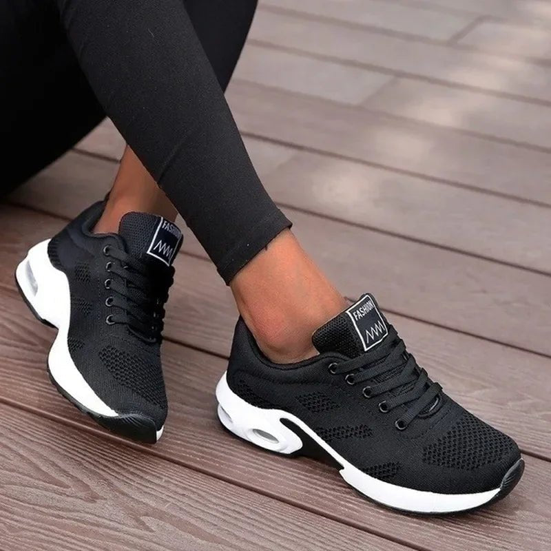 Black athletic shoes with white soles worn by a person on a wooden floor.