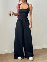 Woman wearing a black jumpsuit holding a drink against a plain background