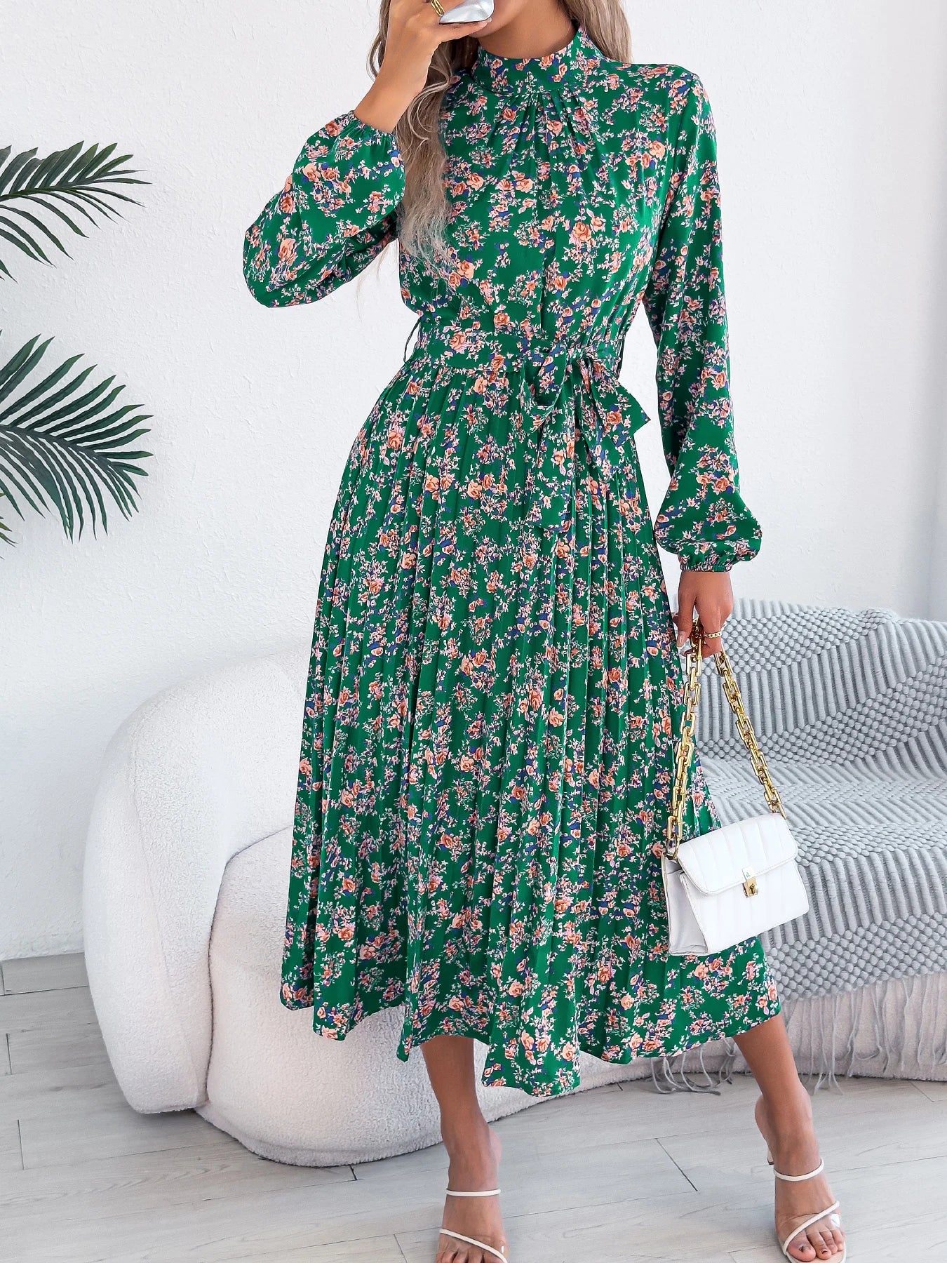 Woman wearing a green floral dress in a room with a white wall and gray sofa.