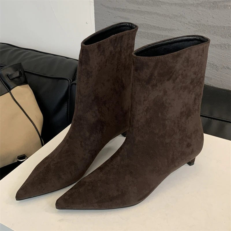 Pair of brown suede ankle boots on a white surface with a neutral background