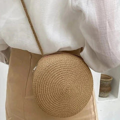 Round woven bag worn over shoulder with a neutral background