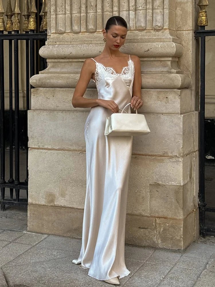 Woman in a white satin evening gown standing against a stone wall.
