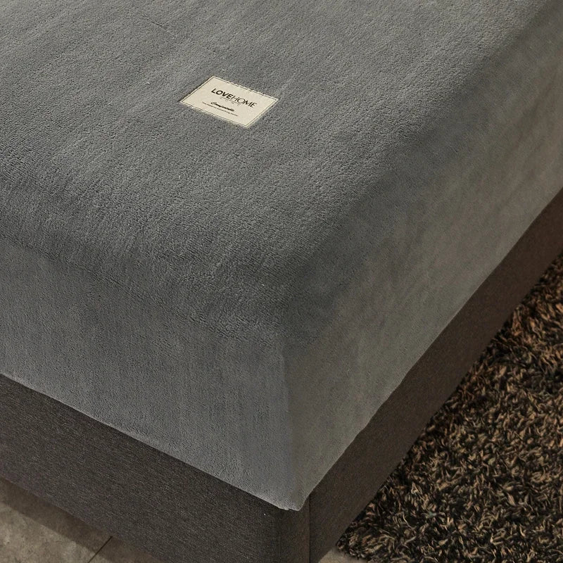 Gray textured mattress cover with a brand label on a wooden bed frame.