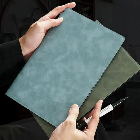 Person holding a teal leather notebook with a pen on a black background