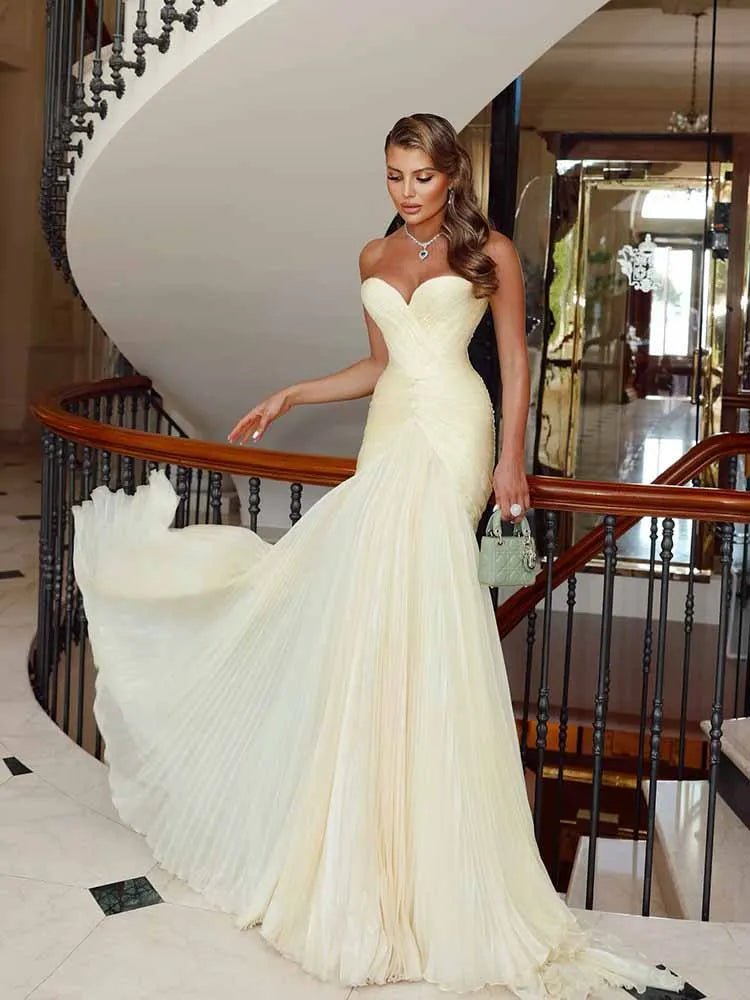 Woman in a white evening gown standing in a luxurious interior setting with a staircase.