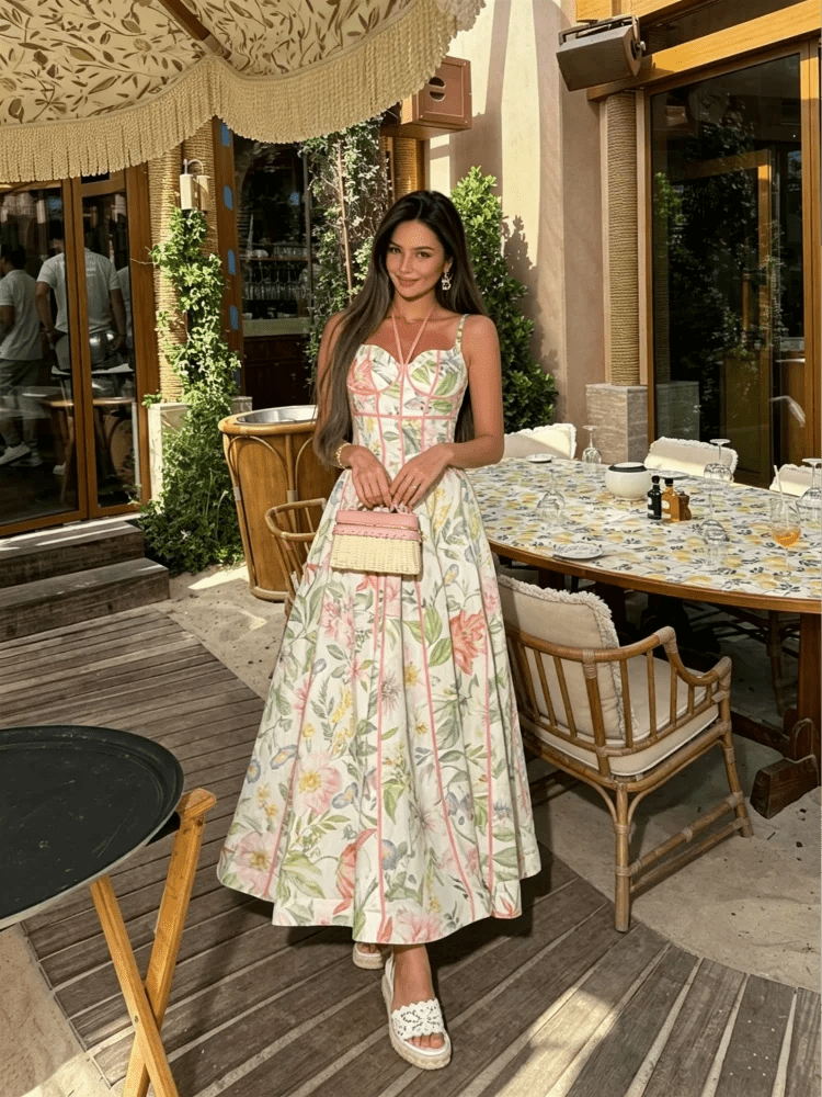 Woman in a floral dress standing in an outdoor setting with tables and chairs.