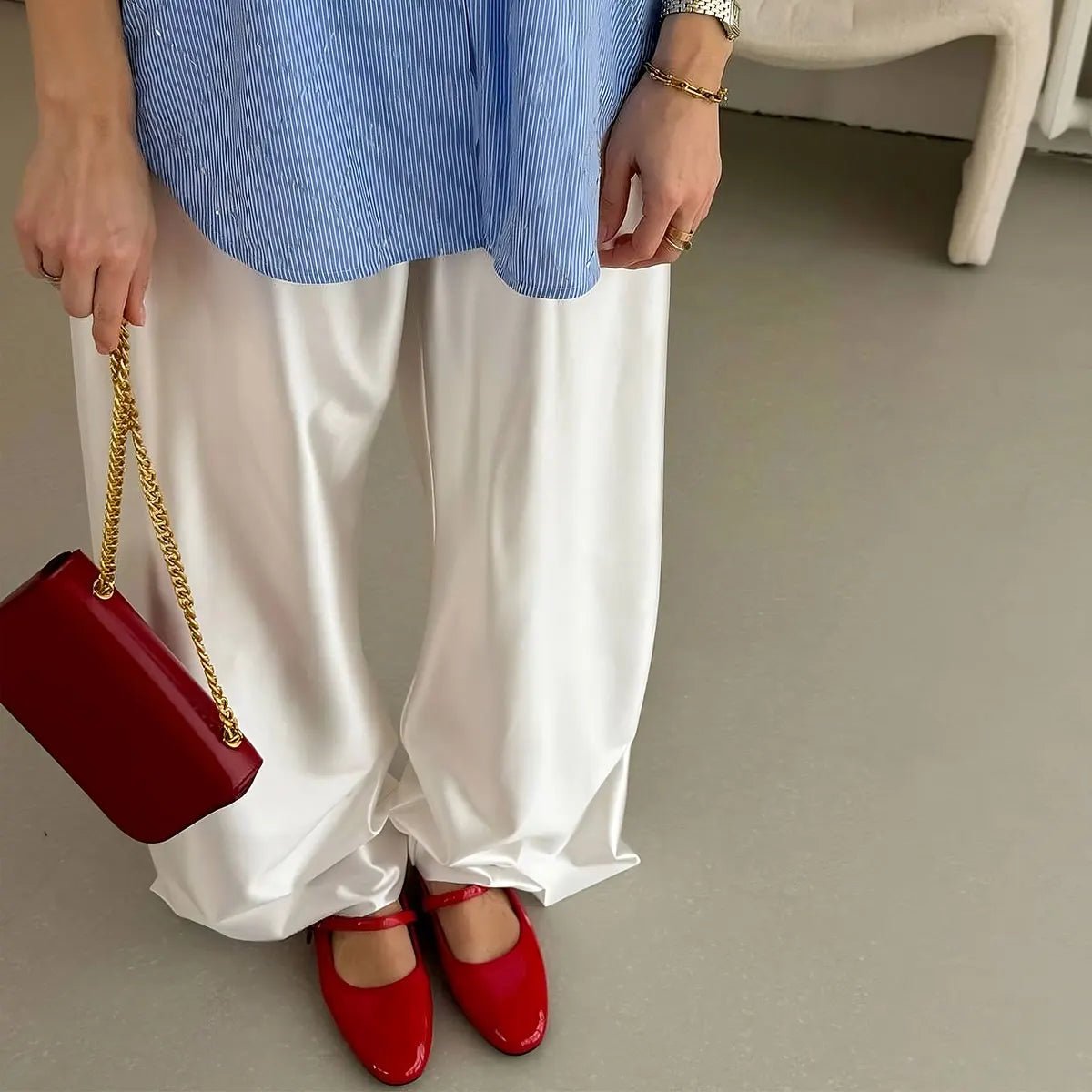 Person wearing a blue shirt, white pants, and red shoes holding a red handbag.