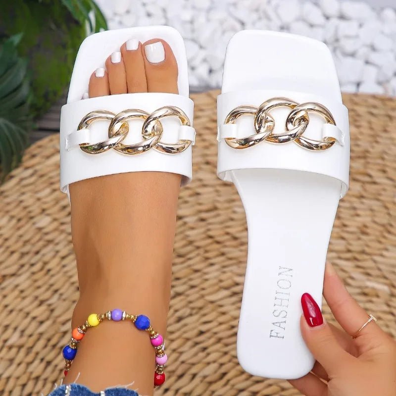 White slides with gold chain design held by a hand on a textured surface.