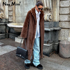 Person wearing a brown fur coat and light blue jeans standing in front of a stone building.