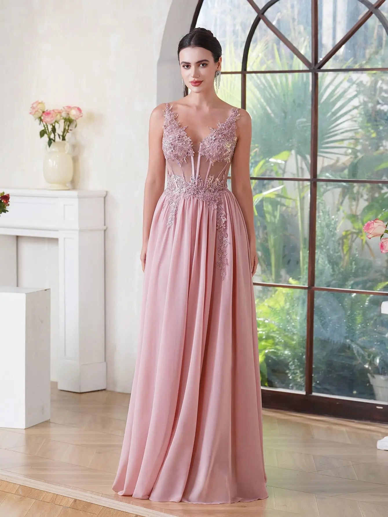 Woman in a pink evening gown standing in a room with a large window and decorative elements.