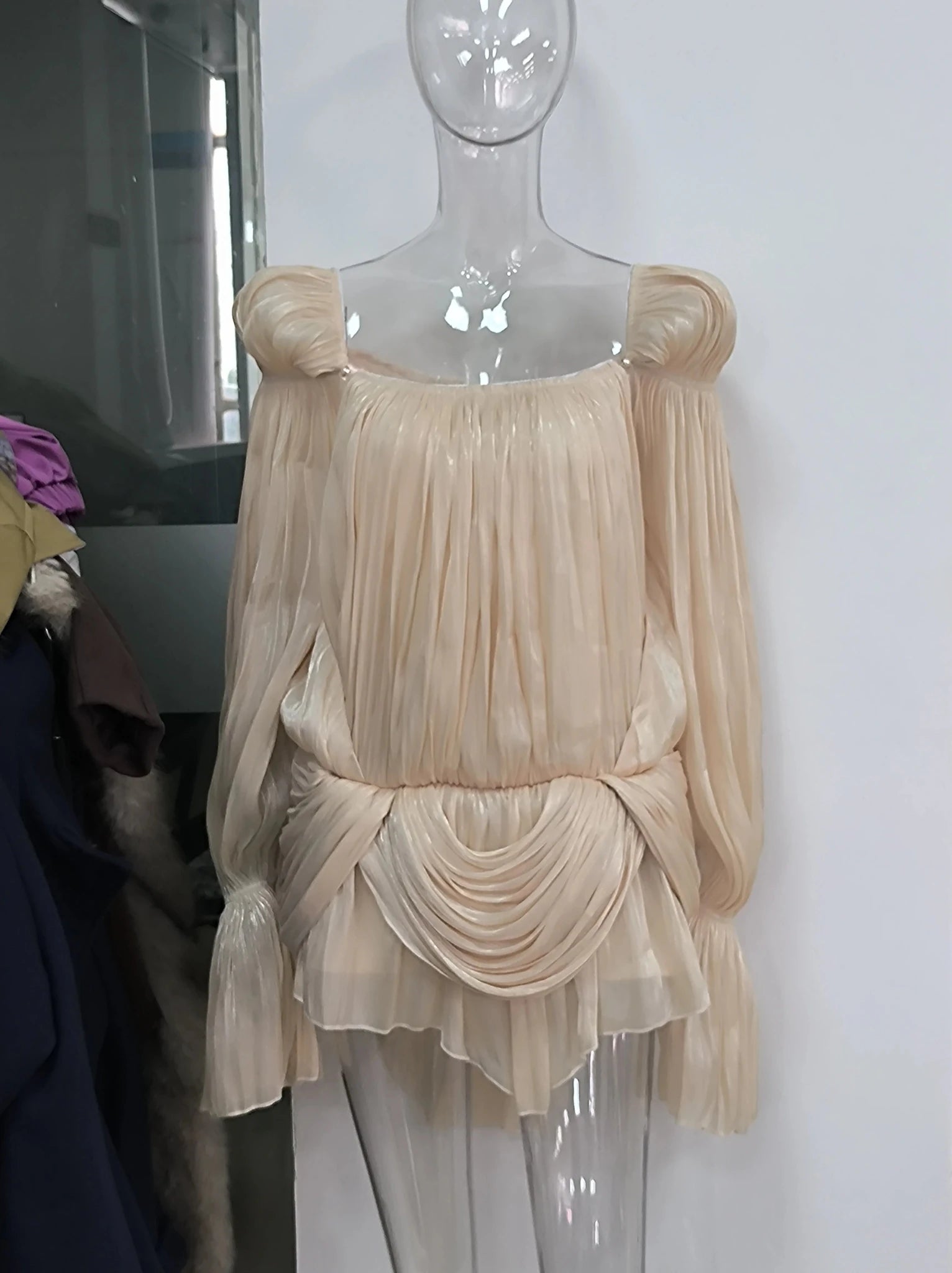Mannequin wearing a beige pleated top with a white background