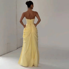 Woman wearing a yellow strapless gown against a plain background