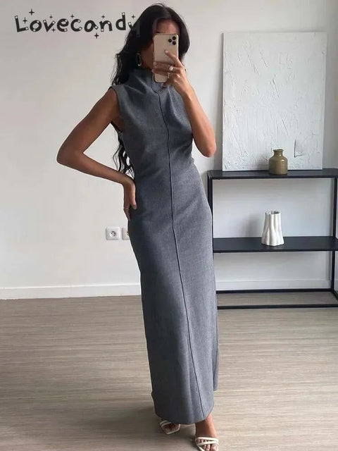 Woman wearing a gray sleeveless dress taking a mirror selfie in a minimalistic room.