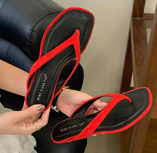 Black sandals with red straps held by a person, brand 'QIAN XIANG FANG' visible.