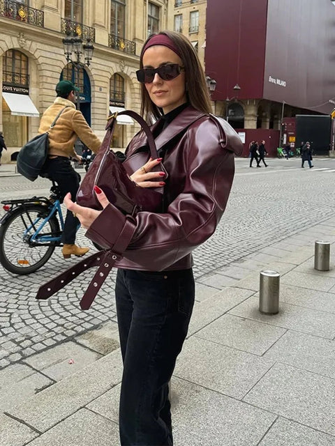 Woman in a maroon leather jacket holding a matching bag on a city street.