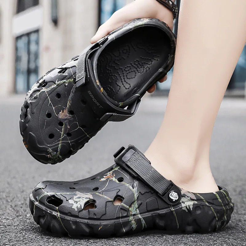 Black camouflage clogs worn by a person on a pavement.