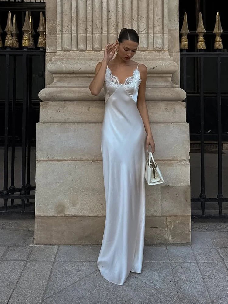 Woman in a white satin dress standing against a stone wall.