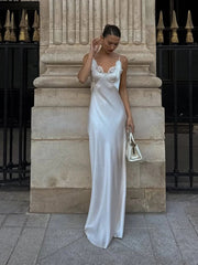Woman in a white satin dress standing against a stone wall.