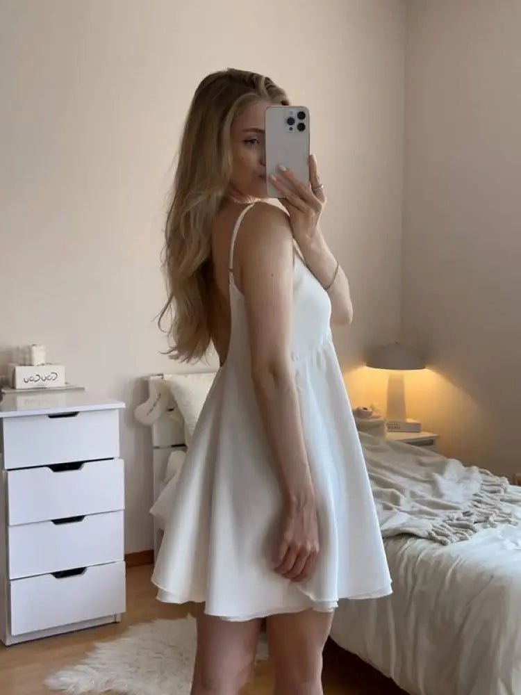Woman taking a mirror selfie wearing a white dress in a bedroom.