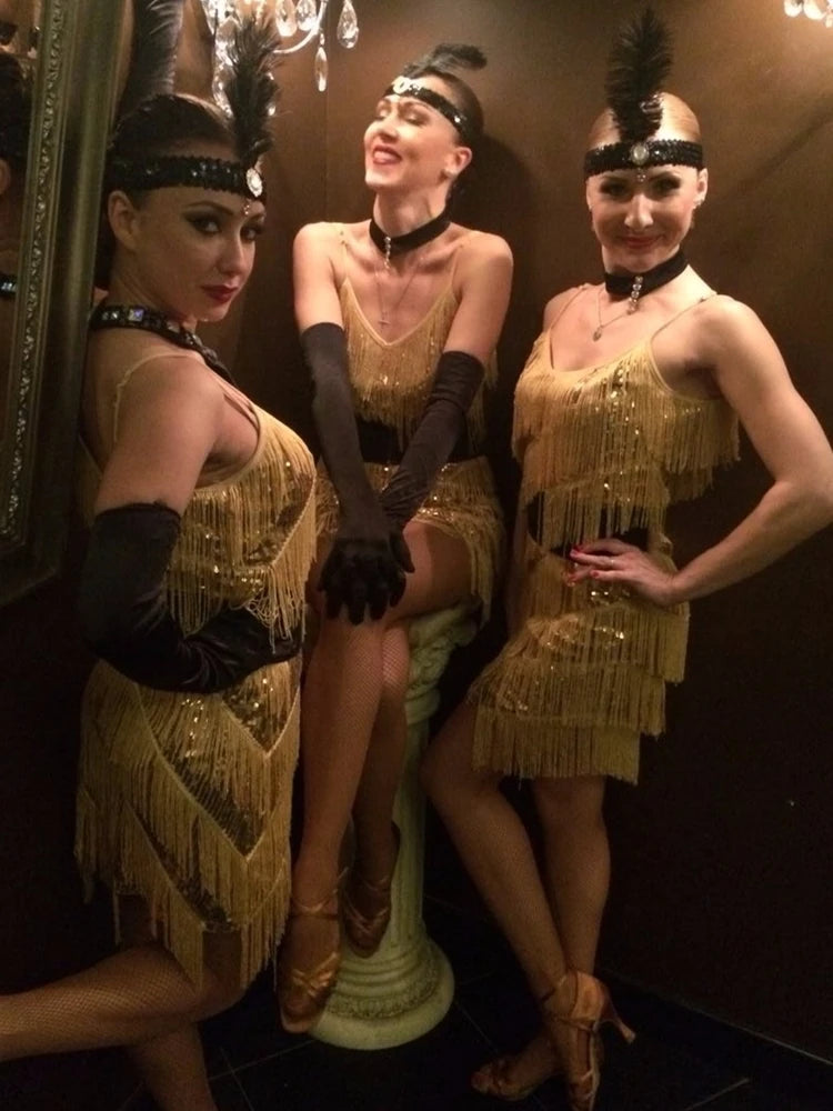 Three women in gold flapper dresses posing in a dimly lit room.