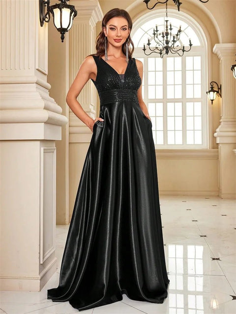 Woman in a black evening gown standing in an elegant interior setting with chandeliers.