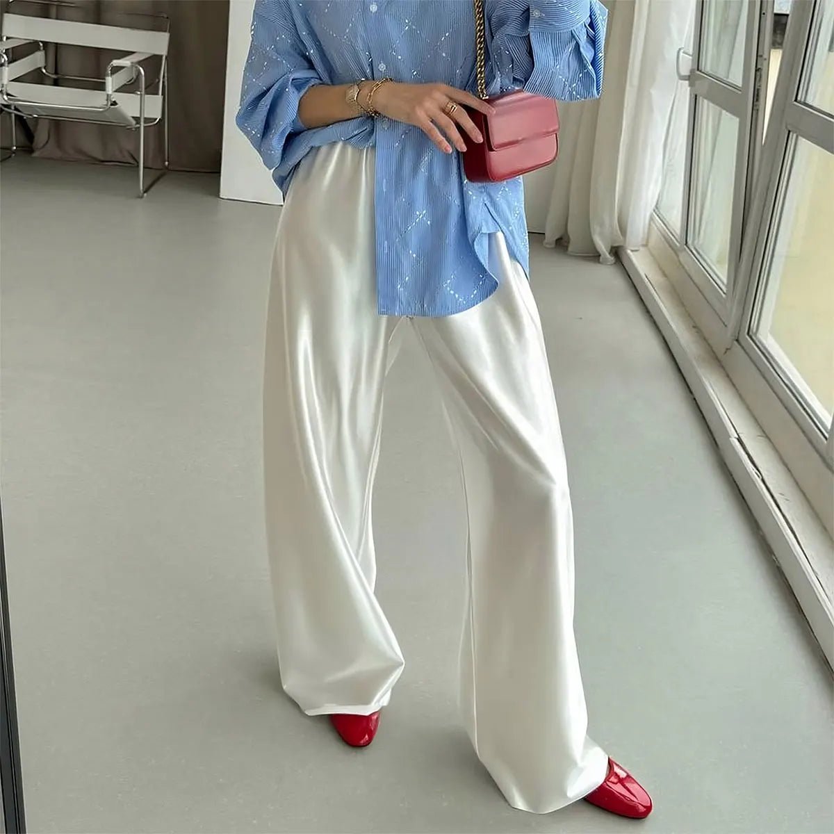 Person wearing a blue top, white pants, and red shoes in a room with a window.