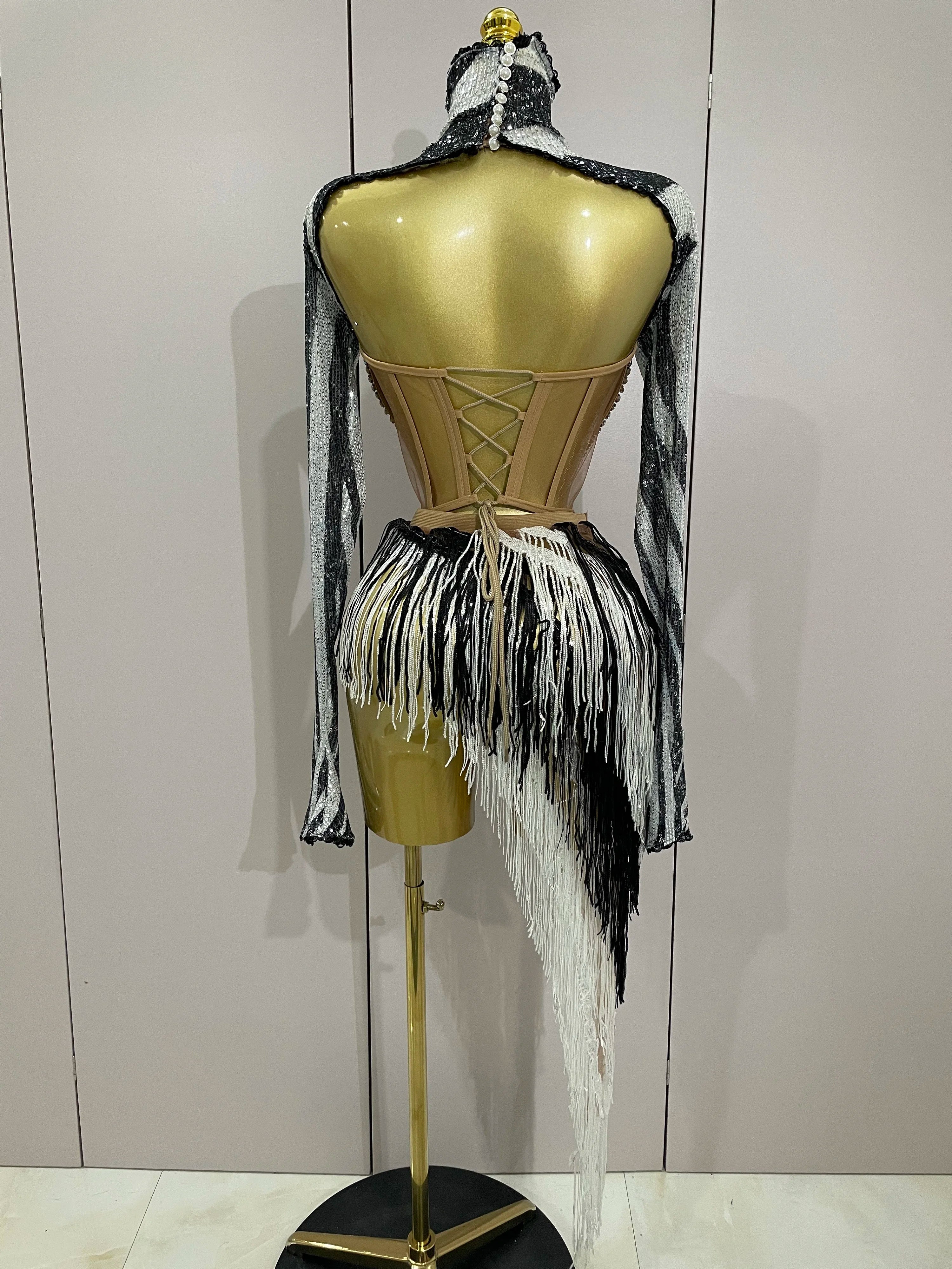 Mannequin wearing a black and white fringe outfit with a gold corset against a plain background