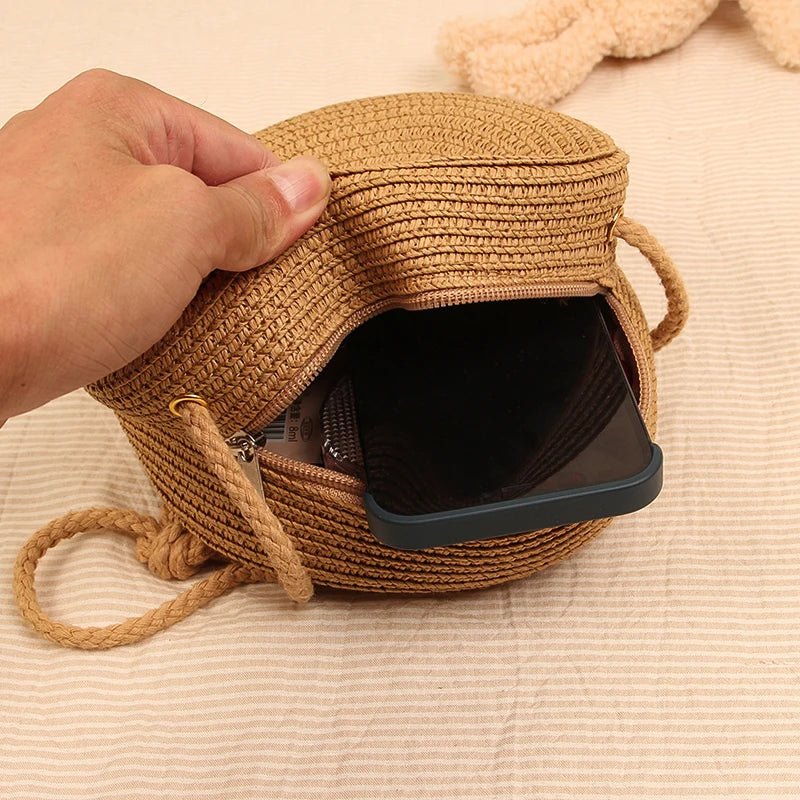 Hand holding a small woven bag with a phone inside on a beige surface