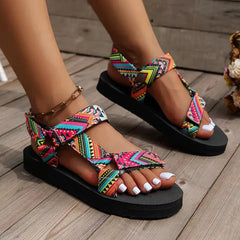 Colorful patterned sandals on feet standing on a wooden floor