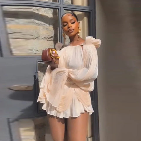 Woman in a beige outfit standing next to a car with a stone wall background