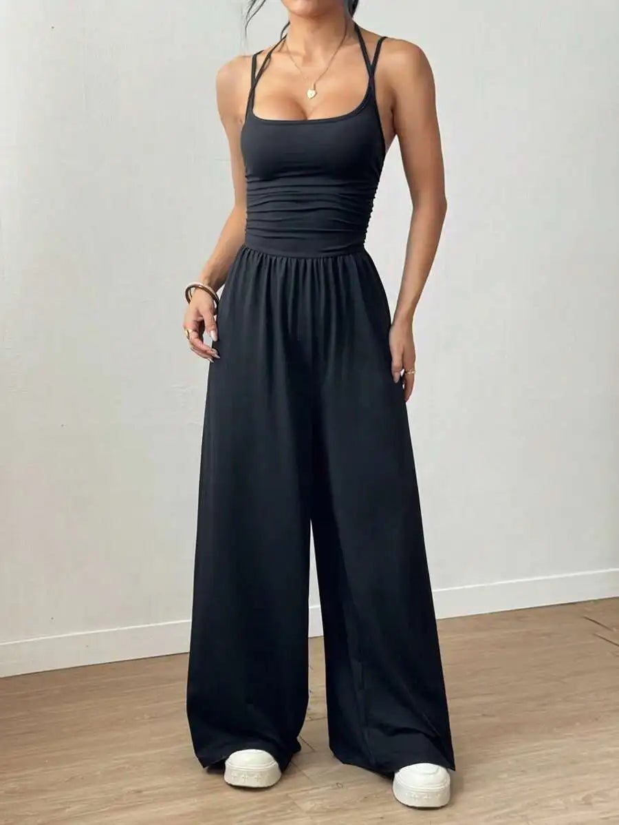 Woman wearing a black jumpsuit standing on a wooden floor with a white wall background