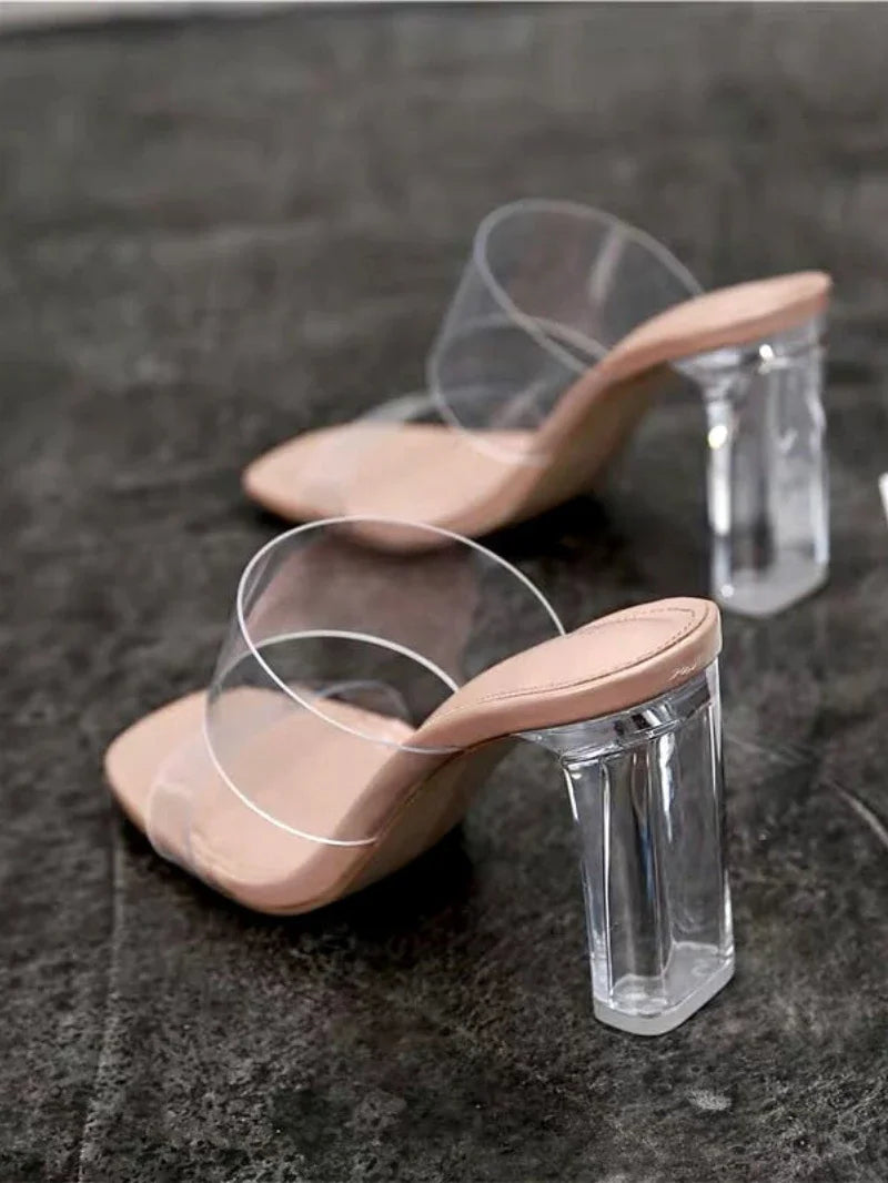 Clear high-heeled shoes with beige soles on a dark textured surface