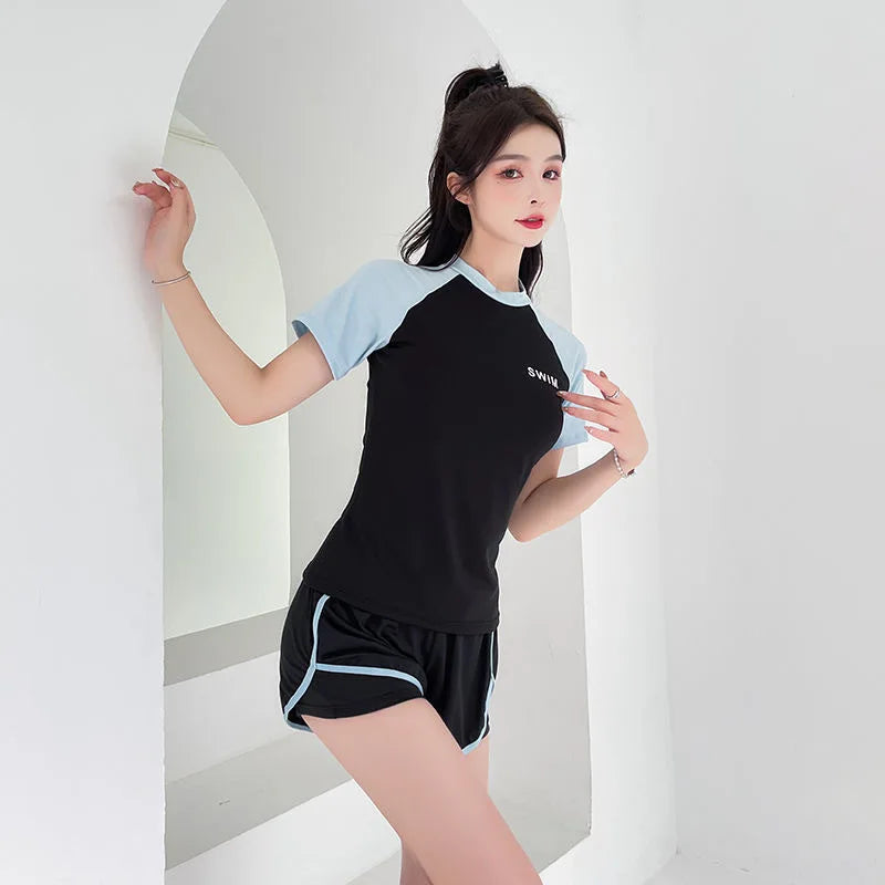 Woman wearing a black and light blue outfit with 'SWIM' text, standing against a white background.