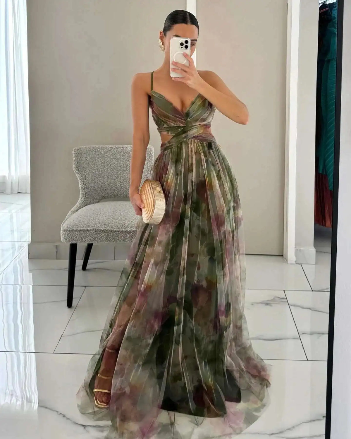 Woman in a floral dress taking a mirror selfie in an indoor setting.