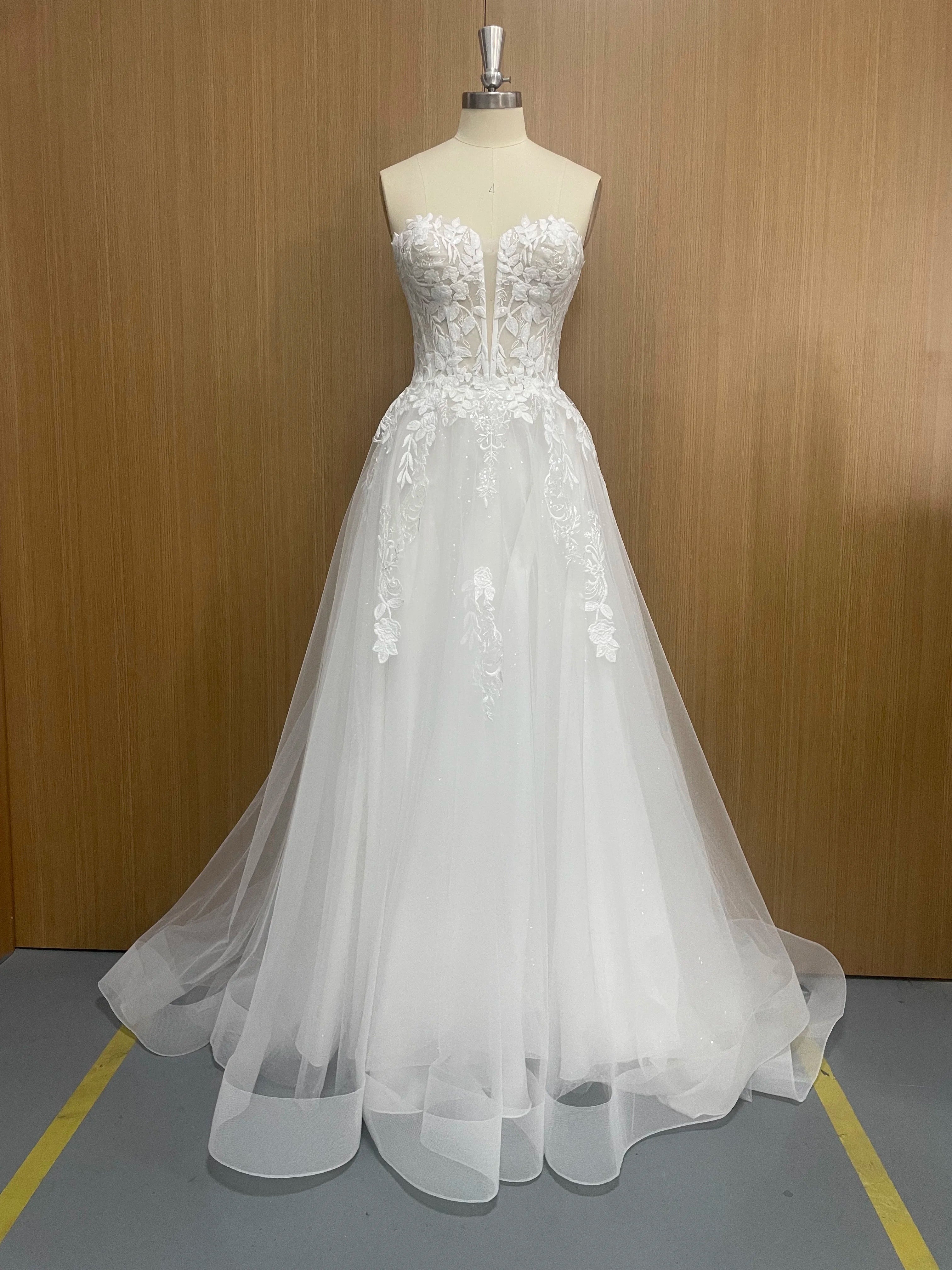 White wedding dress on a mannequin against a wooden wall.