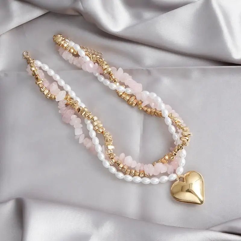 Multistrand necklace with gold and pink beads and a heart pendant on a satin surface