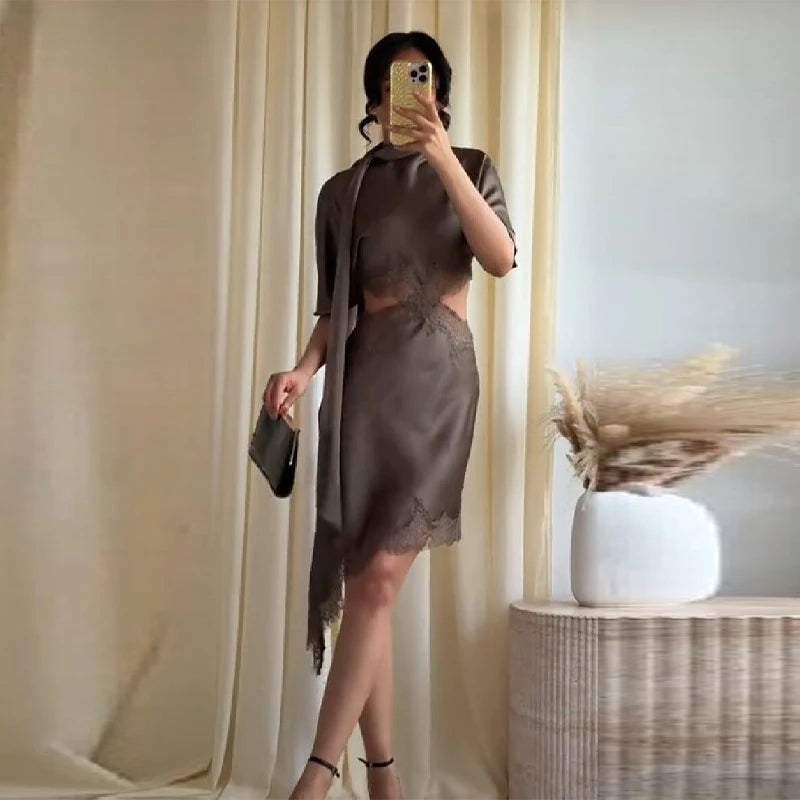 Person wearing a brown dress taking a mirror selfie in a room with beige curtains and a vase.