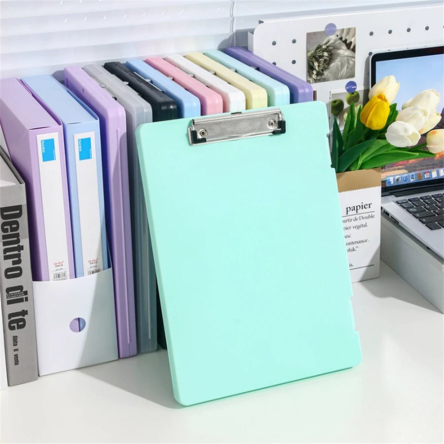 Light blue clipboard on a desk with colorful folders and a laptop in the background