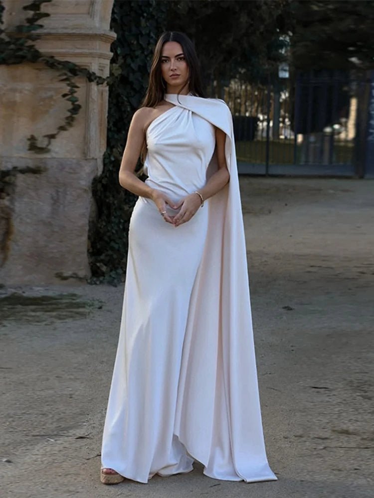 Woman in a white dress standing outdoors with a stone wall and trees in the background