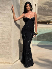 Woman in a black evening gown standing against a stone wall.