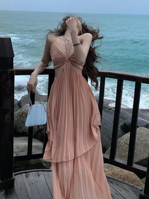 Woman in a pink dress standing on a balcony overlooking the ocean.