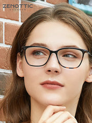 Woman wearing black eyeglasses with a brick wall background, featuring the brand 'Zenottic'.