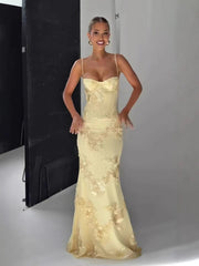 Woman wearing a beige evening gown with floral details in a studio setting.
