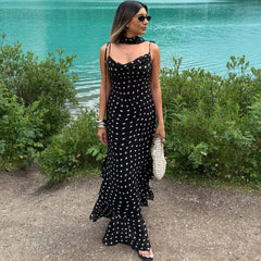 Woman in a black polka dot dress standing by a body of water.