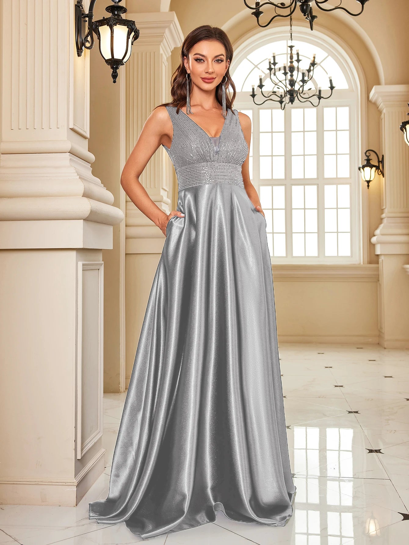 Woman in a silver evening gown standing in an elegant interior setting.