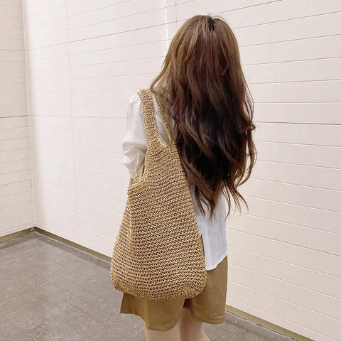 Person wearing a woven beige bag against a white wall