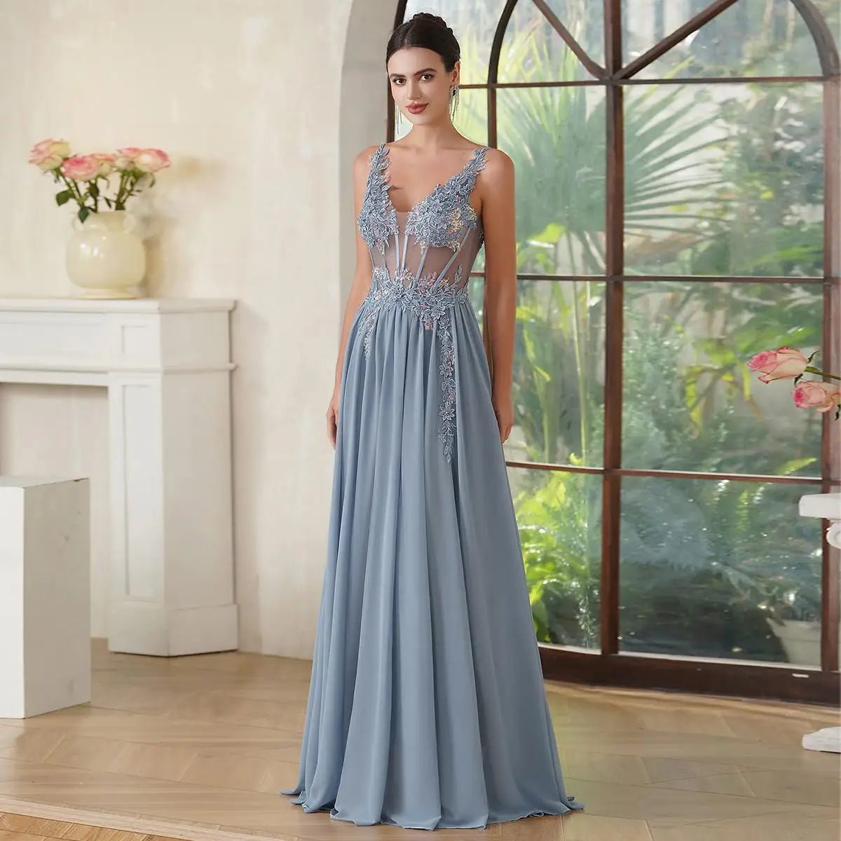 Woman in a light blue evening gown standing in a room with a large window and plants.
