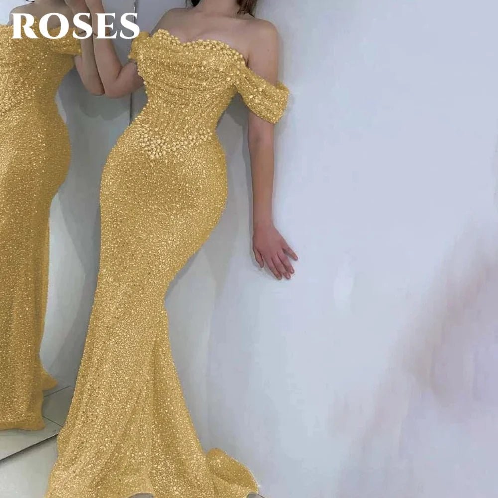 Gold off-shoulder evening gown with a long train on a white background, brand 'ROSES' visible.