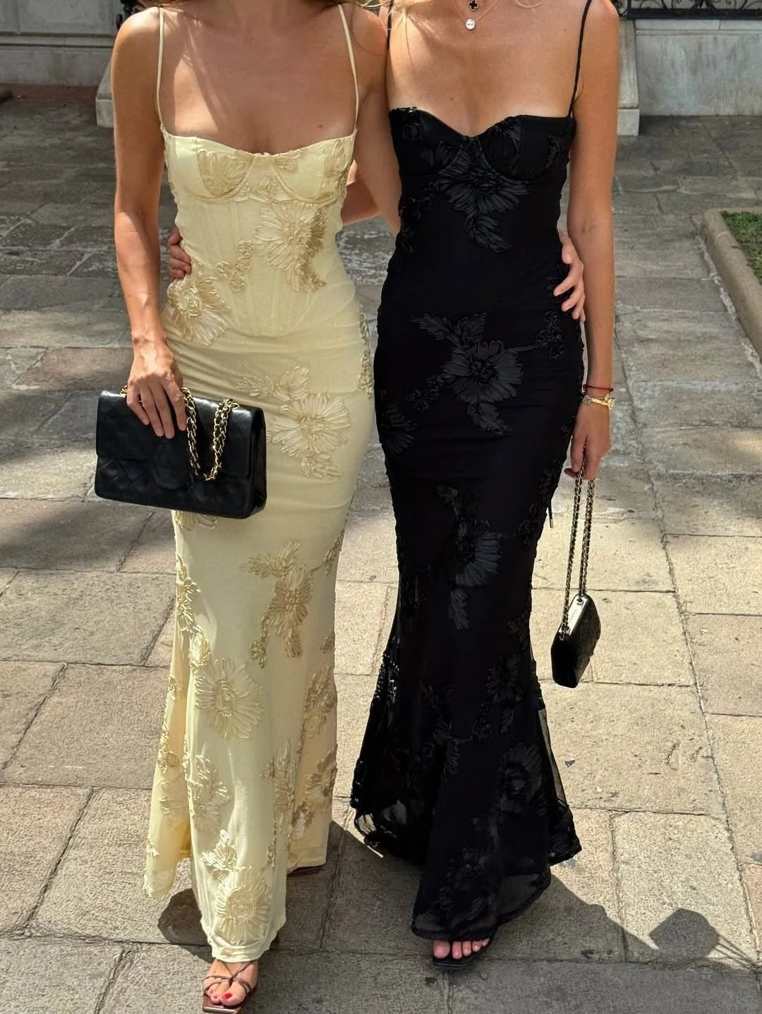 Two women in evening gowns standing on a paved walkway.