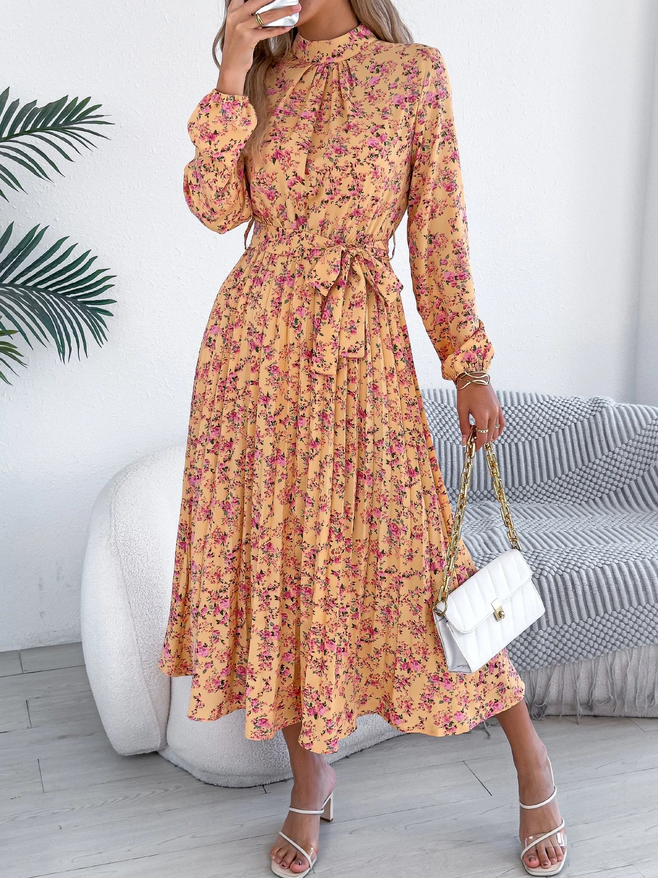 Woman wearing a yellow floral dress in a room with a white wall and gray sofa.